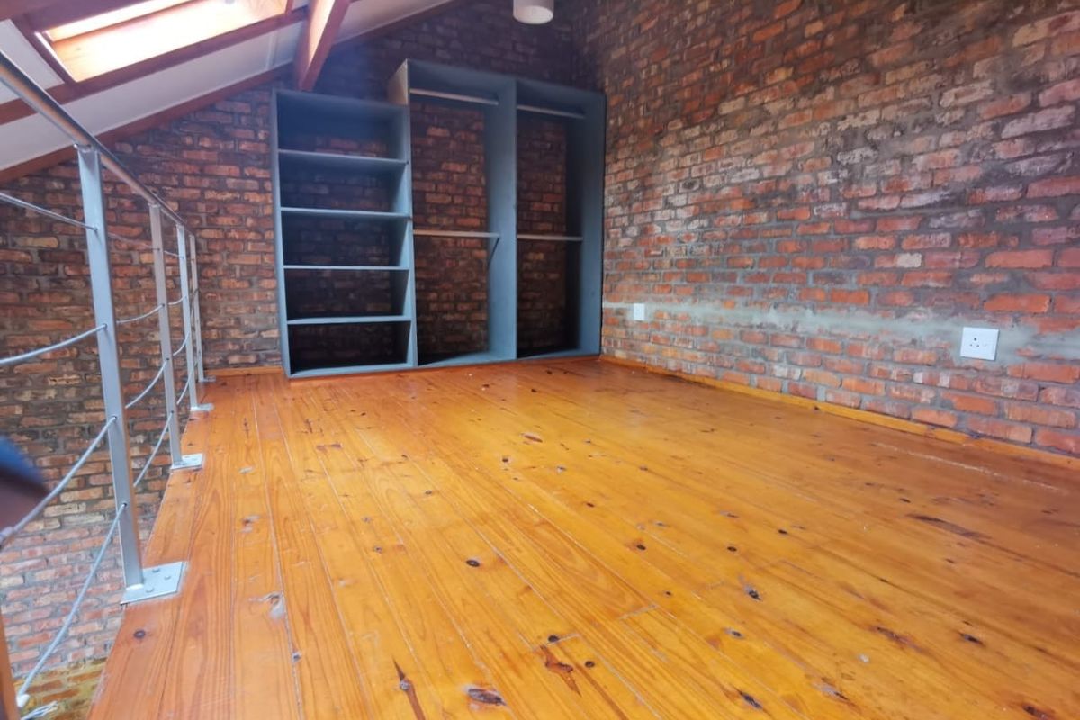 A loft-style bedroom featuring exposed brick walls, polished timber flooring, a skylight, and built-in storage shelving.