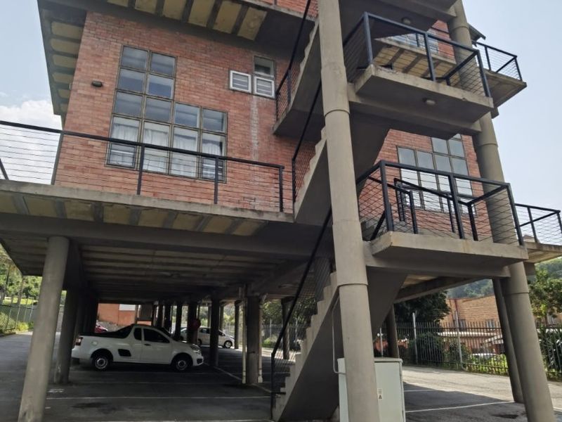 Exterior view of a multi-story apartment building featuring exposed brickwork, concrete structural pillars, external staircases, and covered ground-level parking.