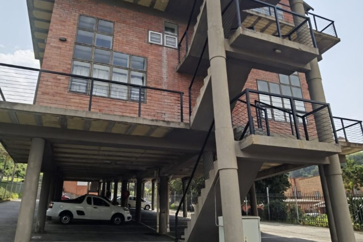 Exterior view of a multi-story apartment building featuring exposed brickwork, concrete structural pillars, external staircases, and covered ground-level parking.