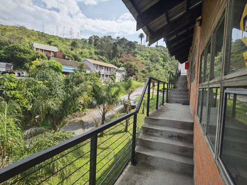 An exterior concrete staircase and balcony walkway featuring metal balustrades and exposed brick walls, overlooking a lush green neighbourhood.