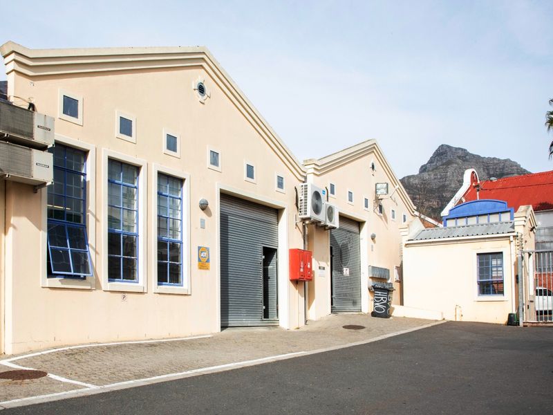Commercial property exterior featuring dual roller shutter doors, mounted air conditioning units, and paved access area with mountain views.