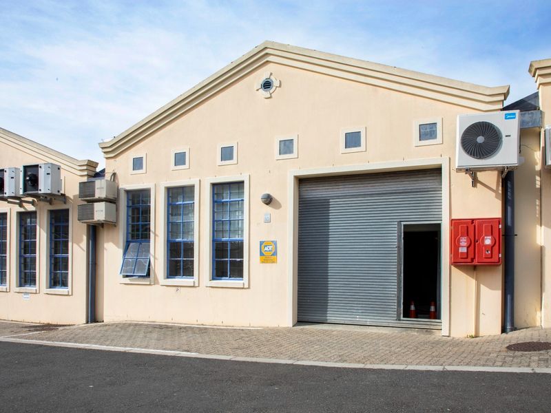 Front elevation of a commercial industrial unit featuring a roller shutter door, multiple air conditioning units, and a fire safety cabinet.