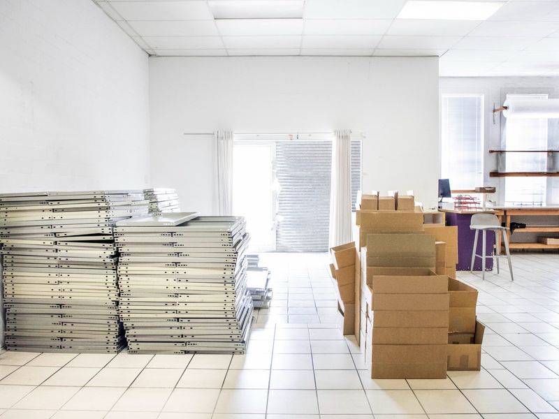 A functional commercial office space featuring tiled flooring, a suspended ceiling, and built-in shelving, currently utilized for storage and workspace.