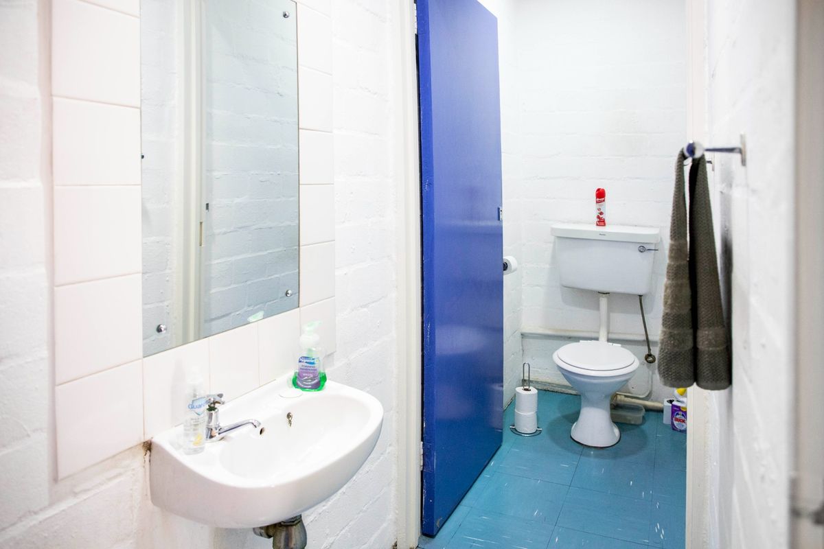 A functional commercial bathroom featuring a wall-mounted basin, toilet, and tiled finishes, presenting an opportunity for modernization.