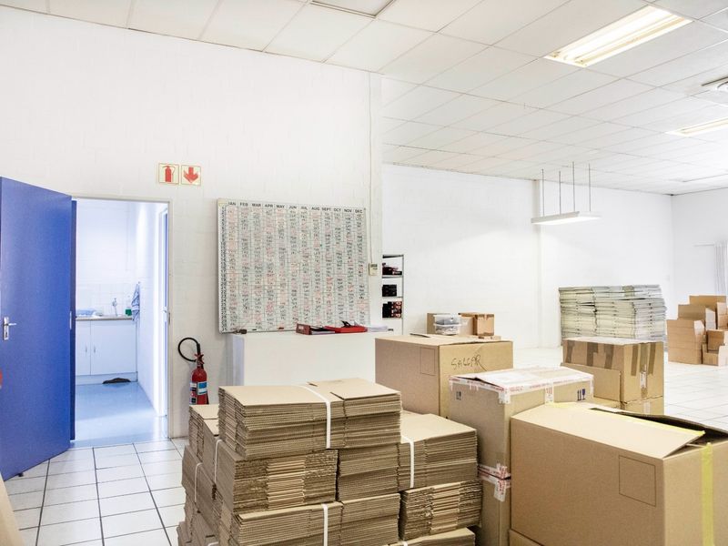 A functional commercial utility space featuring tiled flooring, suspended ceilings, and an adjacent kitchenette area, suitable for storage or administrative use.