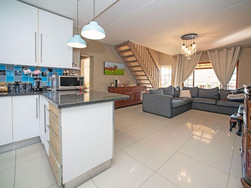 Spacious open-plan living area featuring a modern kitchen with granite countertops, tiled flooring, and a staircase leading to the upper level.