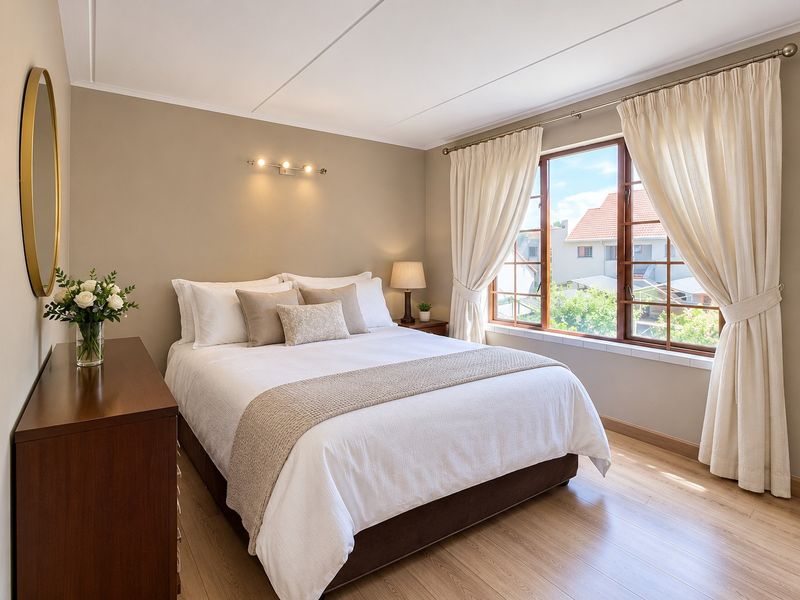 A well-maintained bedroom featuring laminate flooring, neutral wall tones, and large windows that provide natural light and a pleasant exterior view.