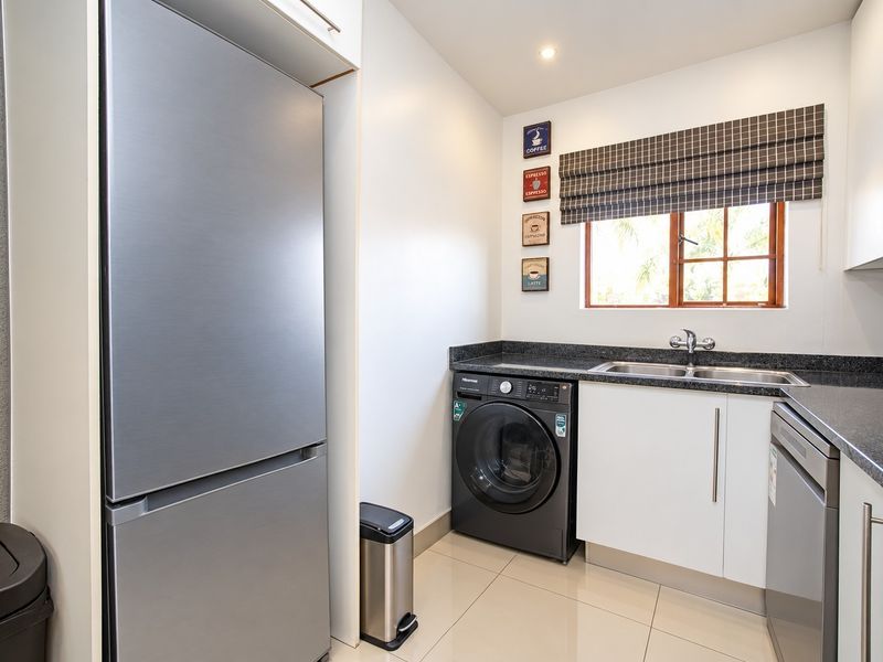 A functional laundry area featuring granite countertops, a stainless steel double sink, built-in cabinetry, and tiled flooring.