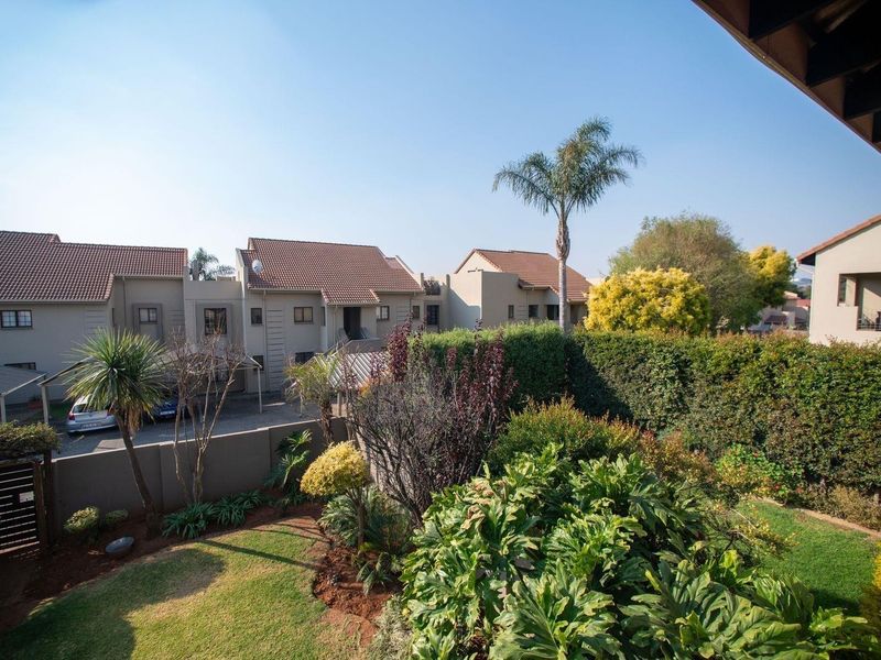 A view of the rear exterior of the apartment complex, featuring a well-maintained garden, boundary walls, and covered parking areas.