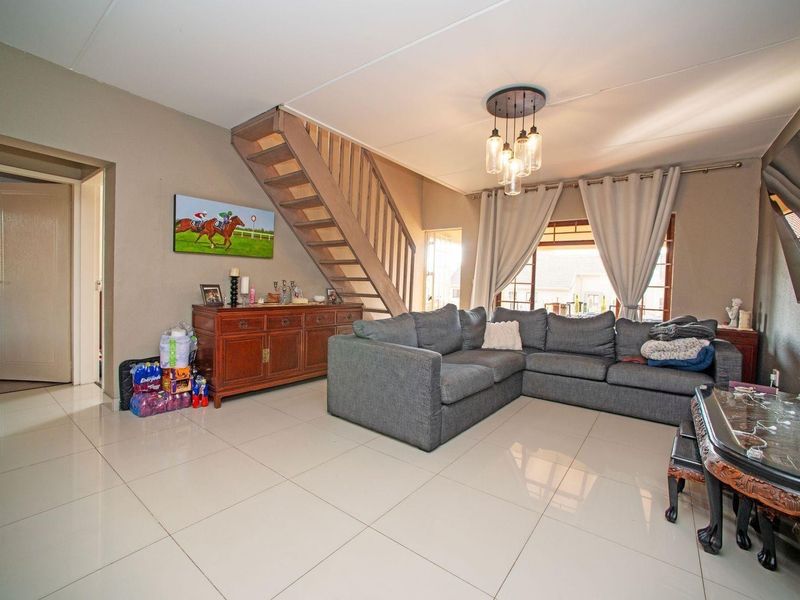 Spacious living room featuring tiled flooring, a central staircase, and modern pendant lighting, offering a functional and open layout.