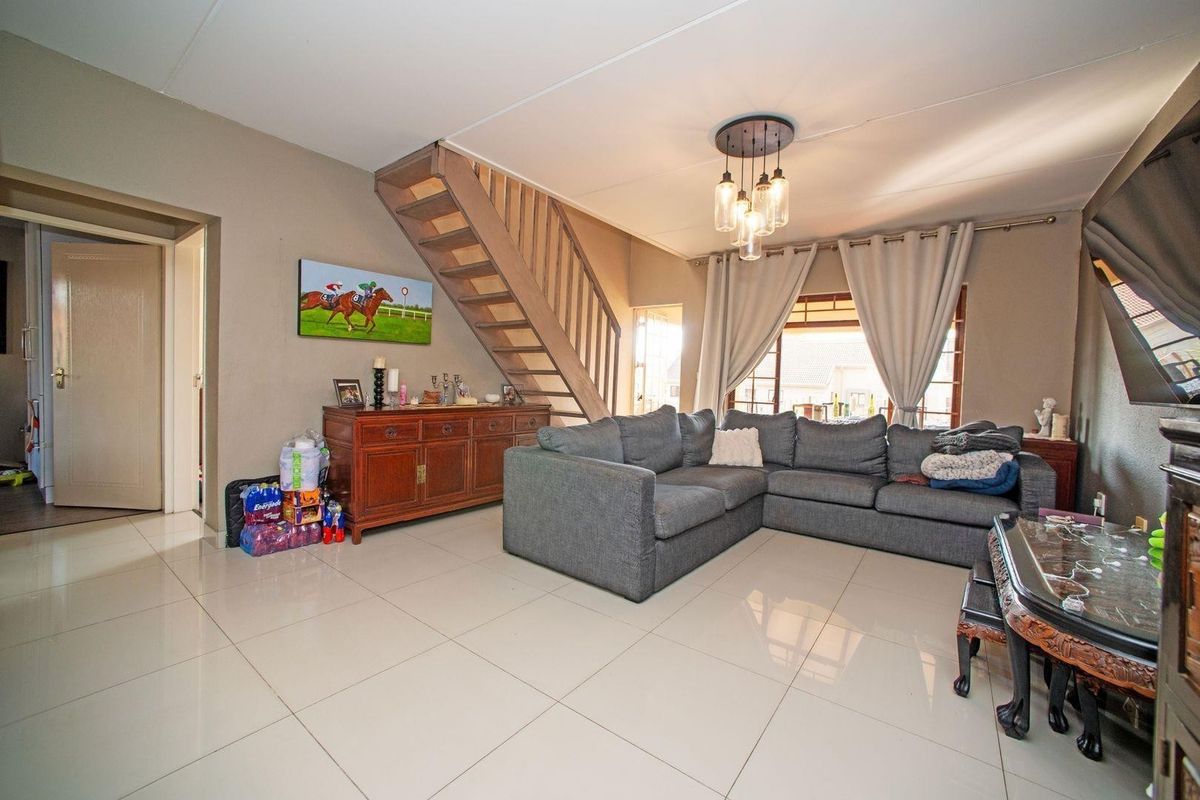 Spacious living room featuring tiled flooring, a central staircase, and modern pendant lighting, offering a functional and open layout.