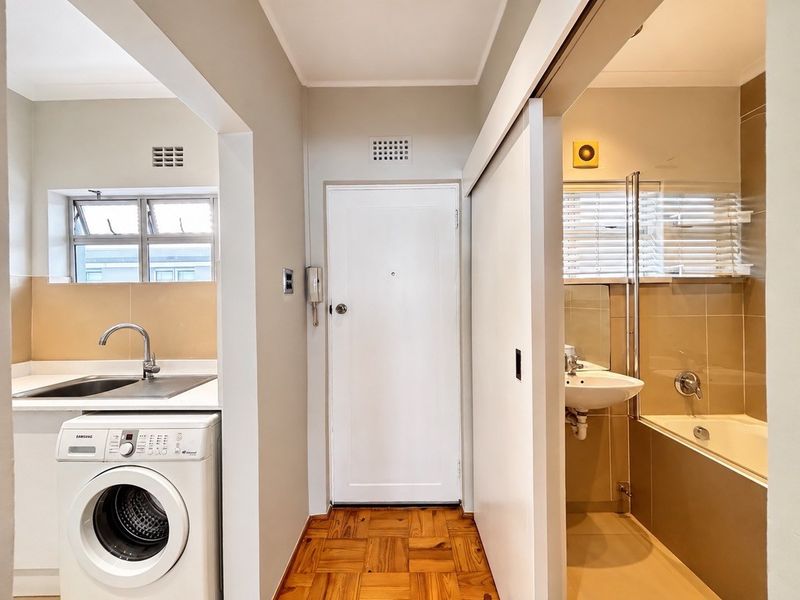 A clean hallway featuring parquet flooring, providing access to an adjacent kitchen area and a bathroom with a sliding door entry.