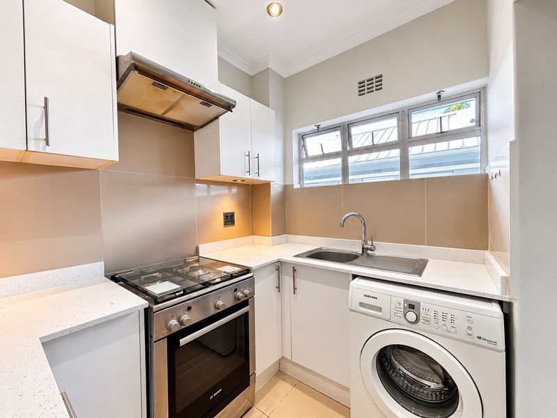 Compact kitchen featuring white cabinetry, quartz countertops, a gas stove with extractor fan, and a stainless steel sink with integrated laundry plumbing.