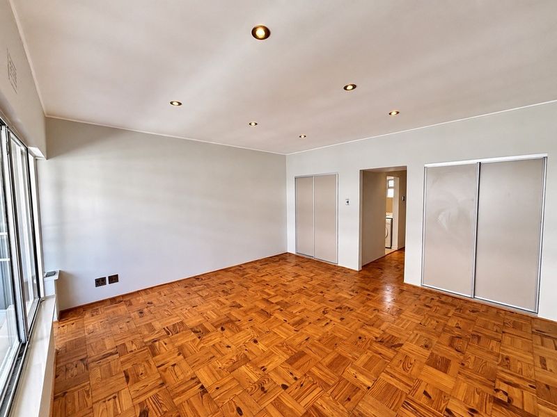 Spacious bedroom featuring classic parquet flooring, built-in cupboards, recessed lighting, and large sliding glass doors providing ample natural light.