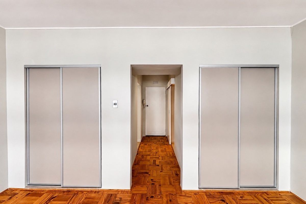 A clean, empty bedroom featuring classic parquet flooring and two built-in sliding door wardrobes, leading into a central hallway.