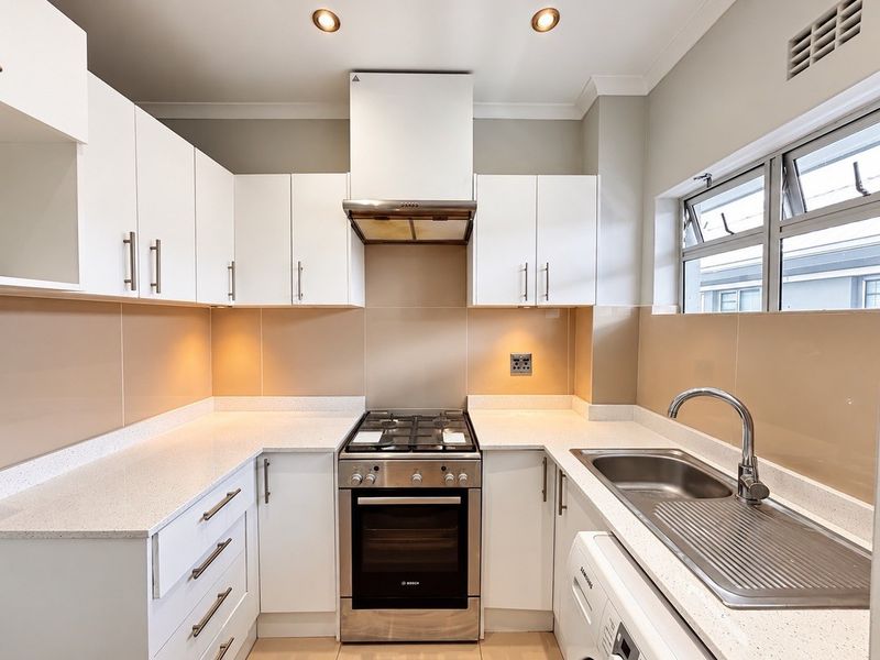 A modern, well-maintained kitchen featuring white cabinetry, stone countertops, stainless steel appliances, and a tiled splashback.