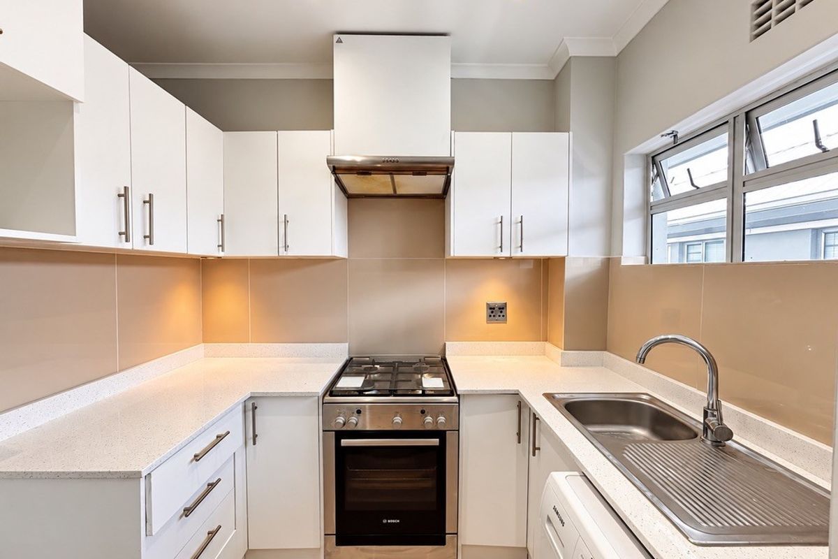 A modern, well-maintained kitchen featuring white cabinetry, stone countertops, stainless steel appliances, and a tiled splashback.