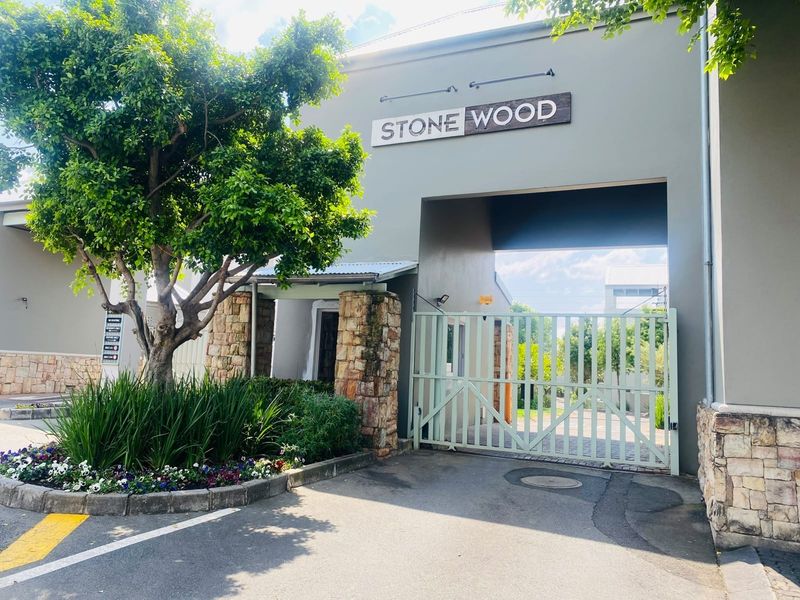 The main entrance gate and facade of the Stone Wood apartment complex, featuring stone masonry accents and secure metal gating.