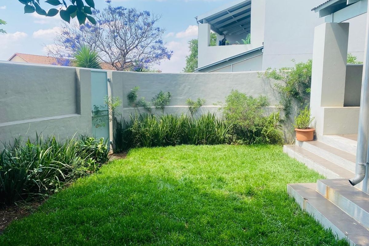 A private rear garden featuring a well-maintained lawn, perimeter boundary wall, and tiled steps leading to the main dwelling.