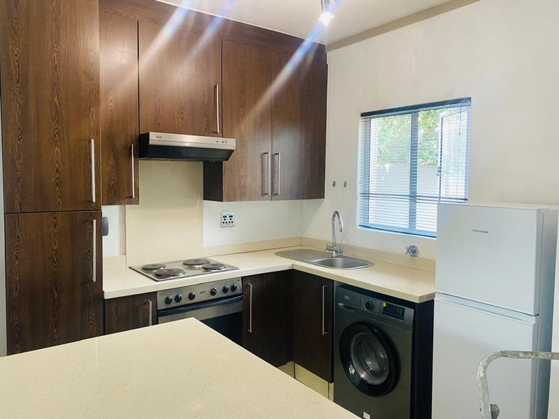 A functional kitchen featuring dark wood cabinetry, stone countertops, an integrated electric hob, oven, extractor fan, and a stainless steel sink.