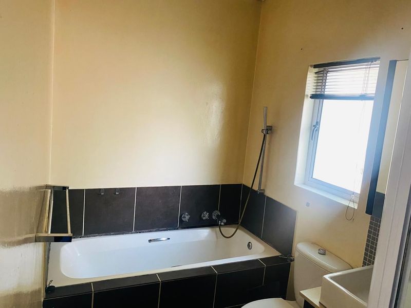 A functional bathroom featuring a built-in bathtub with shower mixer, toilet, and dark tiled splashback, offering potential for cosmetic updates.