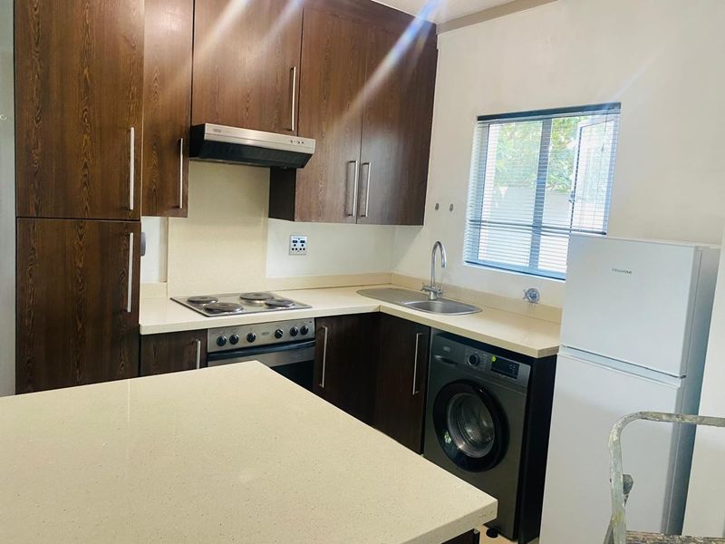 A functional kitchen featuring dark wood cabinetry, stone countertops, integrated appliances, and a stainless steel sink, offering a clean and practical workspace.