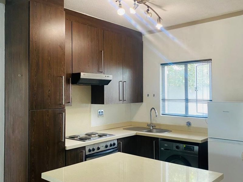 A functional kitchen featuring dark wood cabinetry, stone countertops, built-in oven, extractor fan, and a central island, providing efficient workspace and storage.