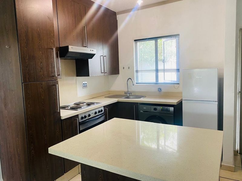 A functional kitchen featuring dark wood cabinetry, stone countertops, a central island, and integrated appliances including an oven, hob, and extractor fan.