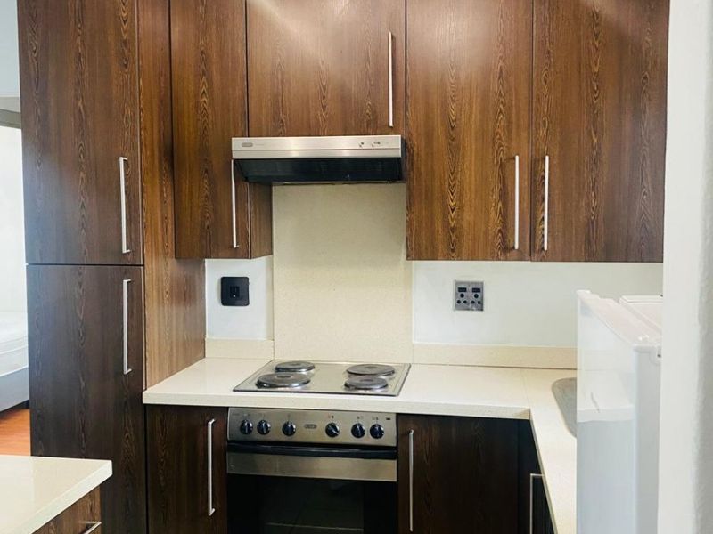 Compact kitchen featuring dark wood cabinetry, stone countertops, built-in oven, electric hob, and tiled flooring.