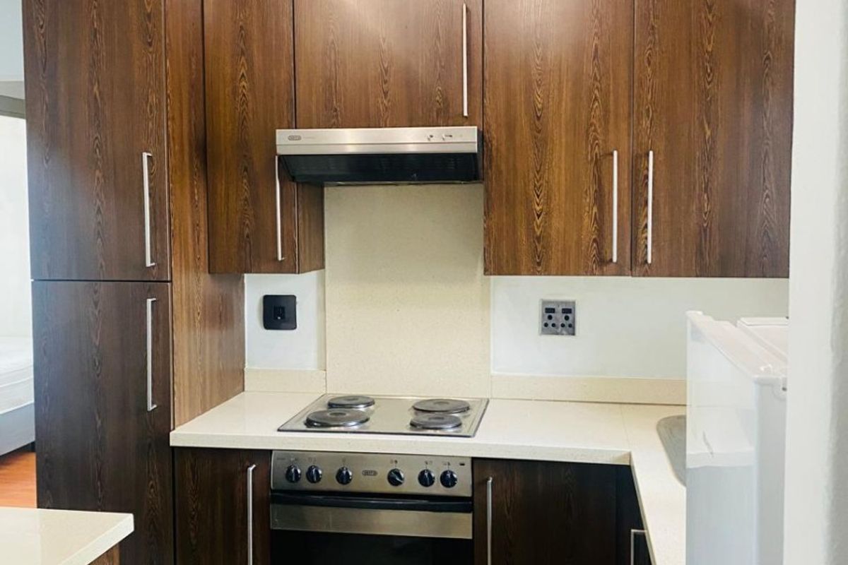 Compact kitchen featuring dark wood cabinetry, stone countertops, built-in oven, electric hob, and tiled flooring.