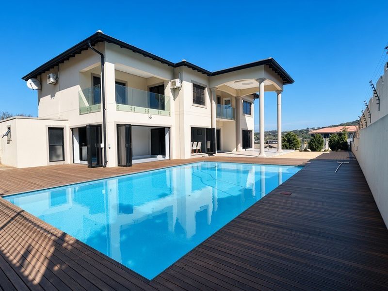 Spacious rear exterior featuring a large swimming pool, modern timber decking, and a covered patio area with glass balustrades and bi-fold doors.
