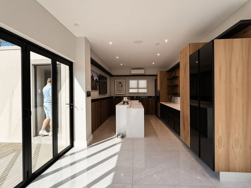 Modern kitchen featuring a stone island, sleek built-in cabinetry, integrated appliances, and large sliding glass doors opening to an outdoor area.