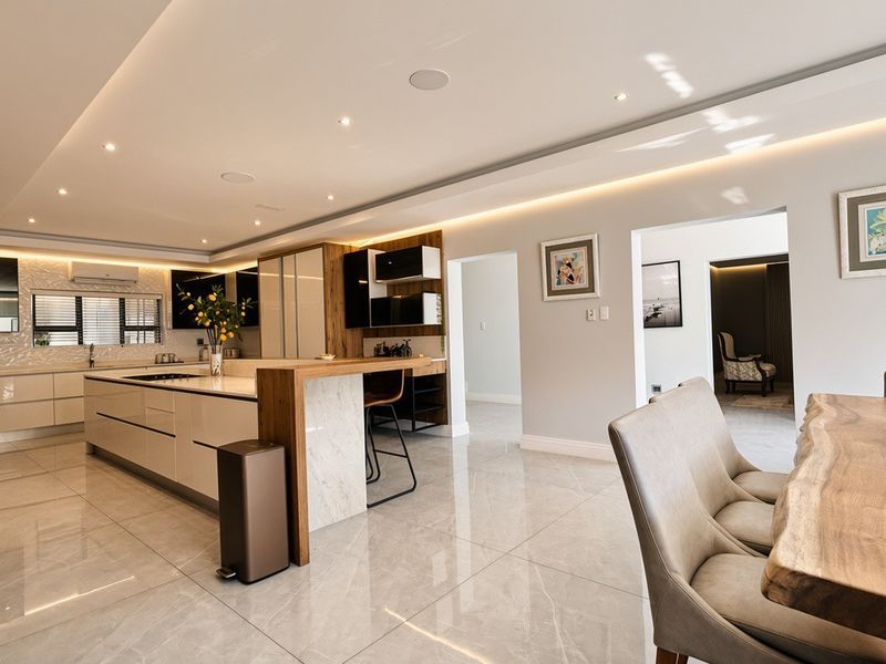 Modern open-plan kitchen and dining area featuring high-gloss cabinetry, a large stone-topped island, and elegant recessed lighting throughout the space.