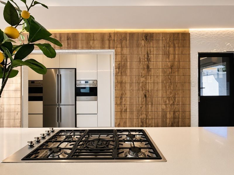 Modern kitchen featuring a central island with a gas cooktop, sleek integrated cabinetry, wood-look wall paneling, and high-end built-in appliances.