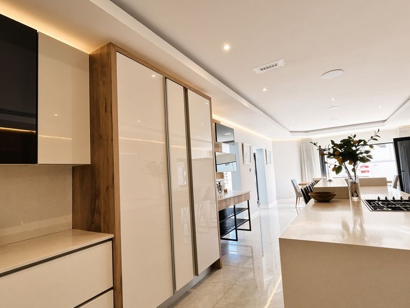 Modern open-plan kitchen and living area featuring high-gloss cabinetry, a large stone island with integrated gas cooktop, and sleek recessed ceiling lighting.