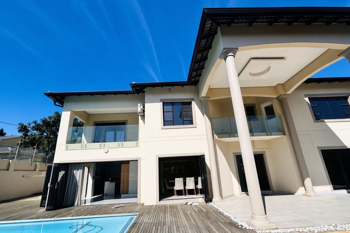 Rear elevation of a modern double-story home featuring a swimming pool, timber decking, covered patio, and glass balustrades with large bi-fold doors.