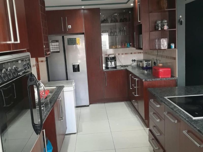 A functional kitchen featuring dark wood cabinetry, granite countertops, built-in oven, hob, and modern recessed ceiling lighting with tiled flooring.