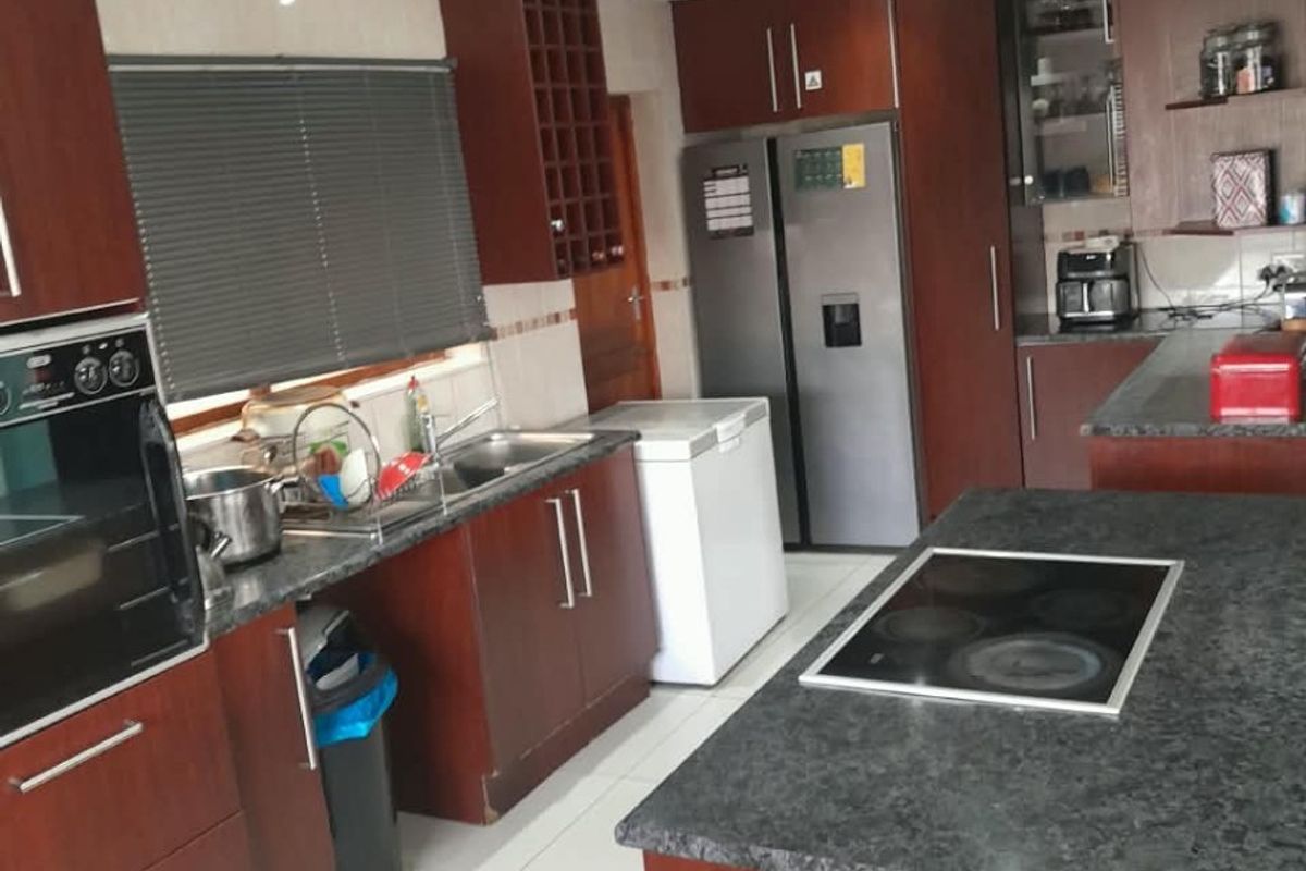 Spacious kitchen featuring dark wood cabinetry, granite countertops, a central island with an integrated hob, and modern recessed ceiling lighting.