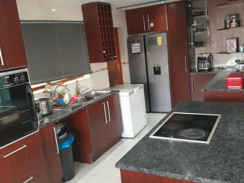 Spacious kitchen featuring dark wood cabinetry, granite countertops, a central island with an integrated hob, and modern recessed ceiling lighting.