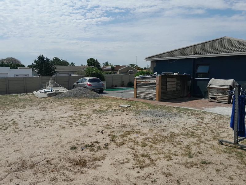 Rear exterior view of the property featuring a swimming pool, paved patio, and a large unlandscaped yard area requiring maintenance and development.