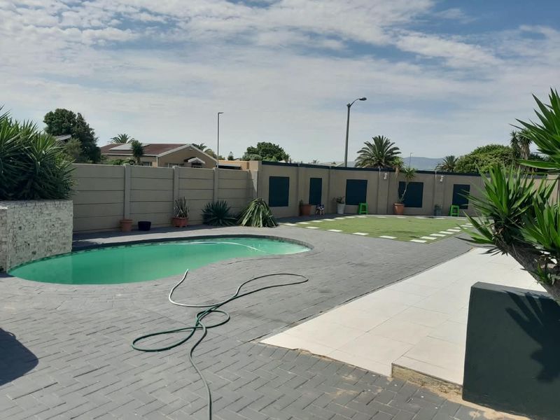 Outdoor pool area featuring a kidney-shaped swimming pool, paved patio surround, and a low-maintenance artificial lawn enclosed by a boundary wall.