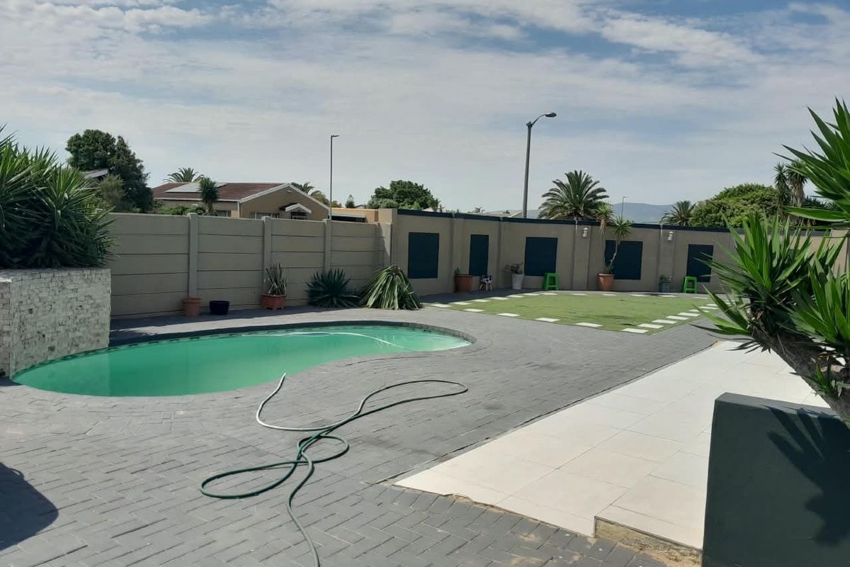 Outdoor pool area featuring a kidney-shaped swimming pool, paved patio surround, and a low-maintenance artificial lawn enclosed by a boundary wall.