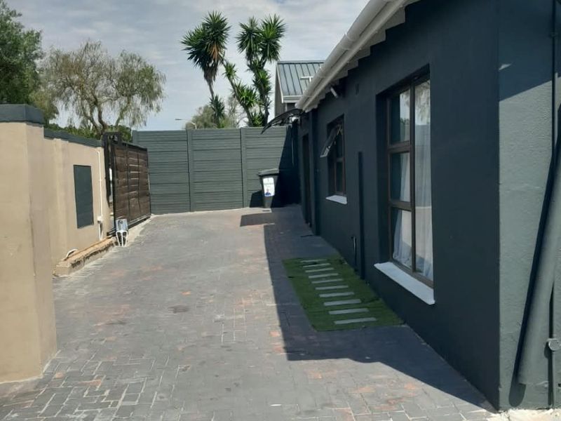 A side view of the property featuring a paved driveway, boundary walls, and exterior building finishes including guttering and downpipes.