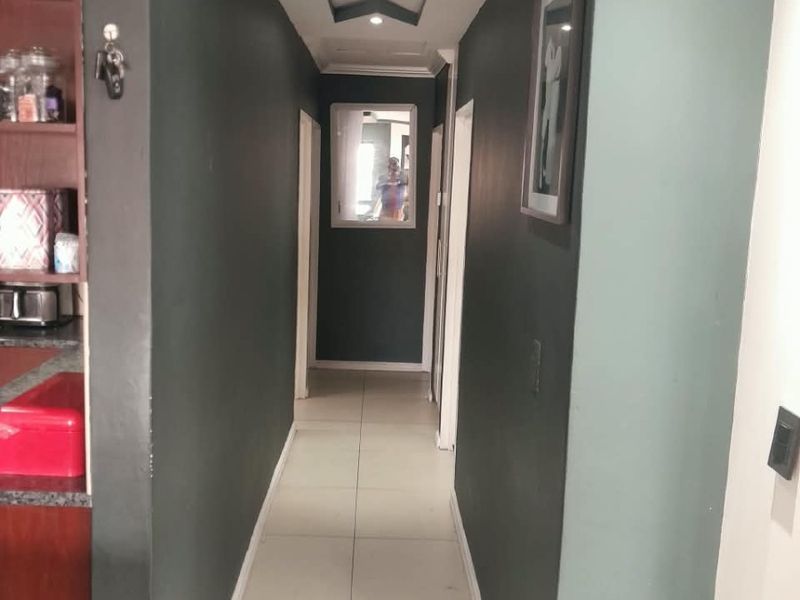 A well-lit hallway featuring modern dark-toned walls, tiled flooring, and recessed ceiling architectural details, providing a clean transition between living spaces.