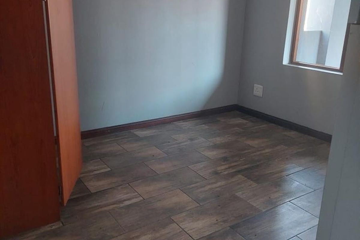An empty bedroom featuring wood-look tiled flooring, a built-in cupboard, and neutral wall finishes, offering a blank canvas for personalization.