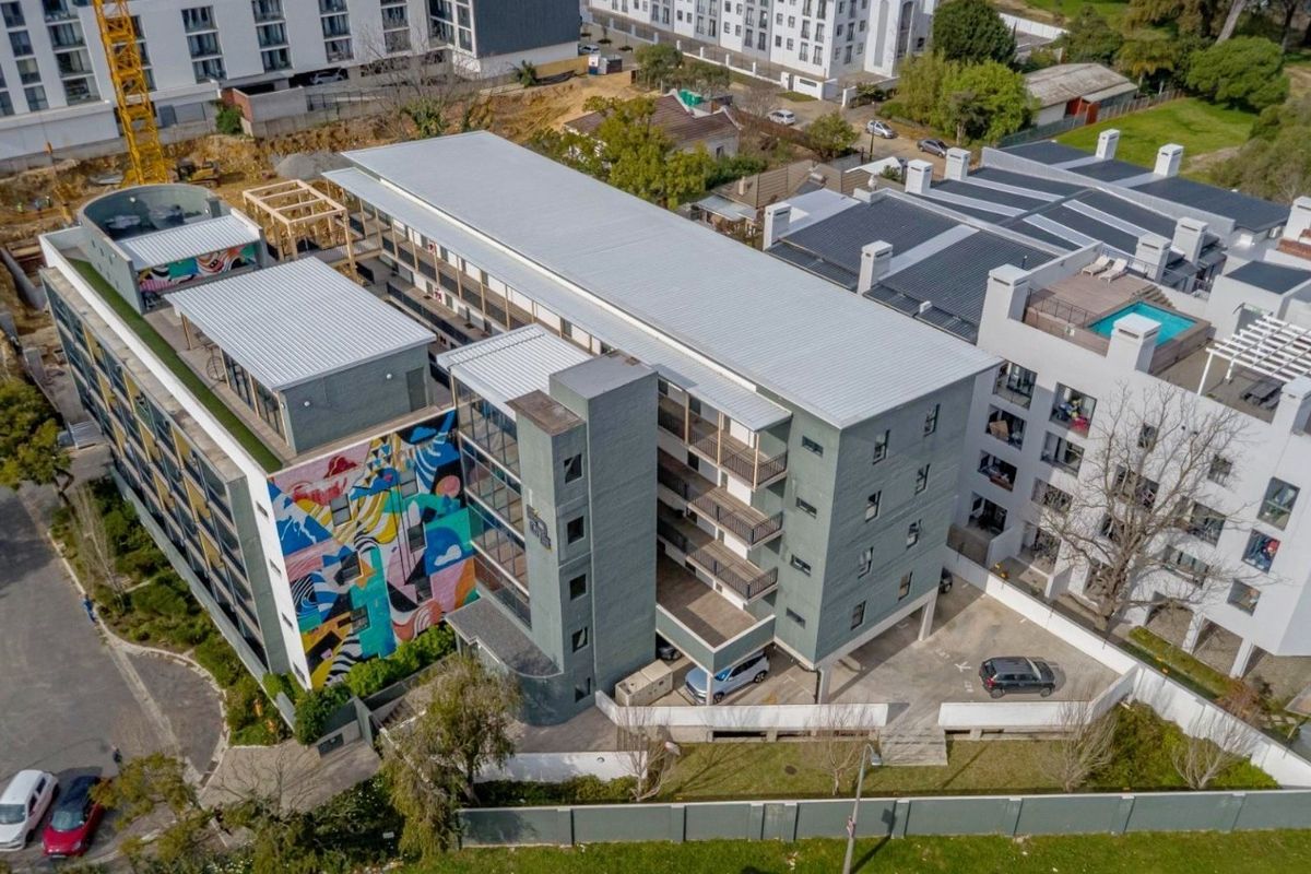 Aerial view of a multi-story residential apartment building featuring a large exterior mural, metal roofing, and ground-level parking facilities.