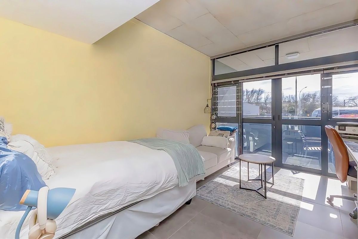A bedroom featuring tiled flooring, large glass sliding doors providing natural light, and a drop ceiling, offering a functional space with potential for modernization.