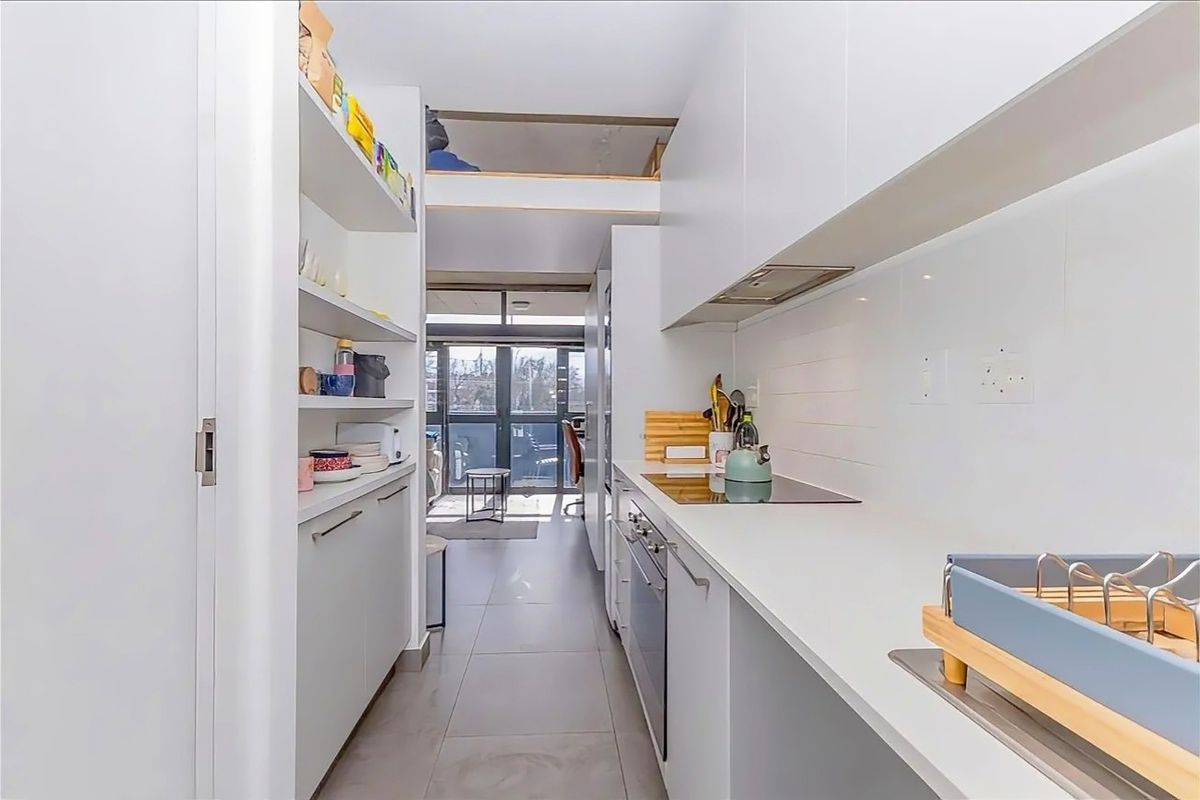 Modern galley-style kitchen featuring sleek white cabinetry, stone countertops, integrated appliances, and a clean subway tile backsplash.