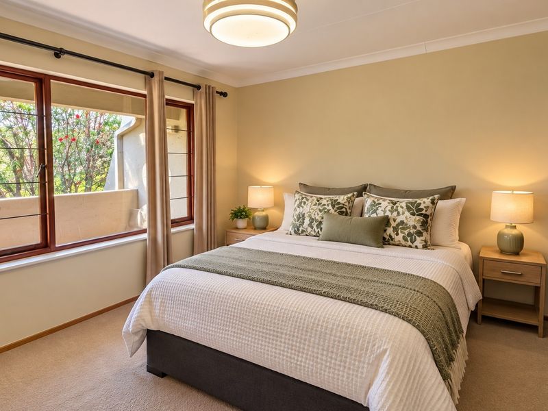 A well-maintained bedroom featuring neutral walls, carpet flooring, a large window with natural light, and a built-in wardrobe.