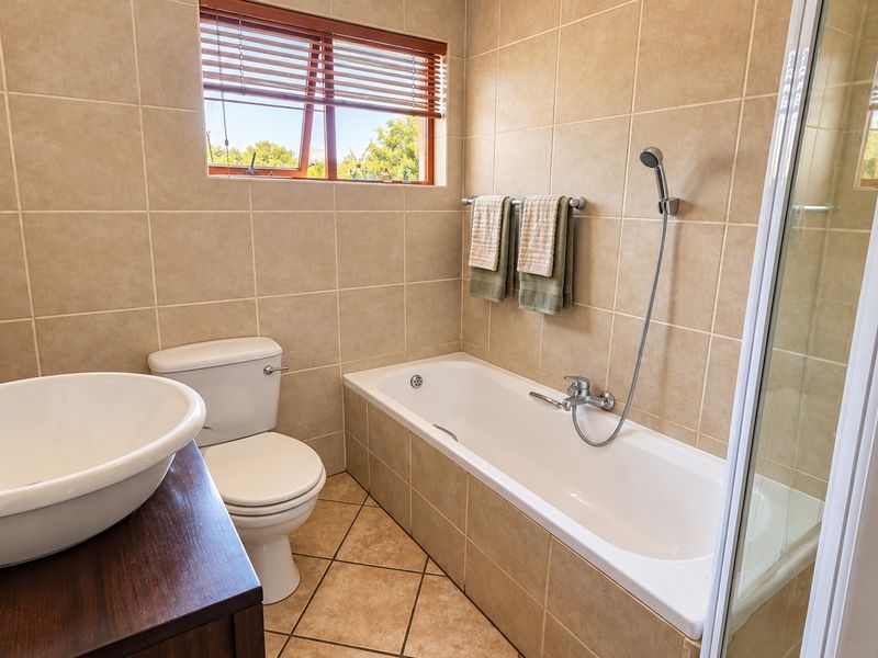 A well-maintained bathroom featuring neutral wall tiles, a built-in bathtub with shower mixer, a modern basin, and a separate shower enclosure.